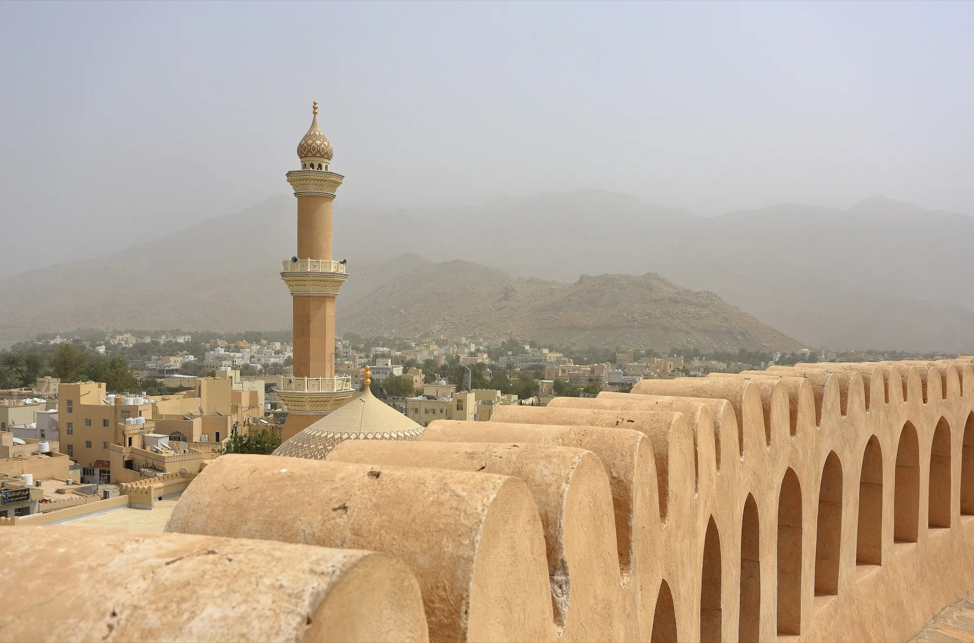 View over Nizwa from the fort wall, with a minaret and mountains in the haze