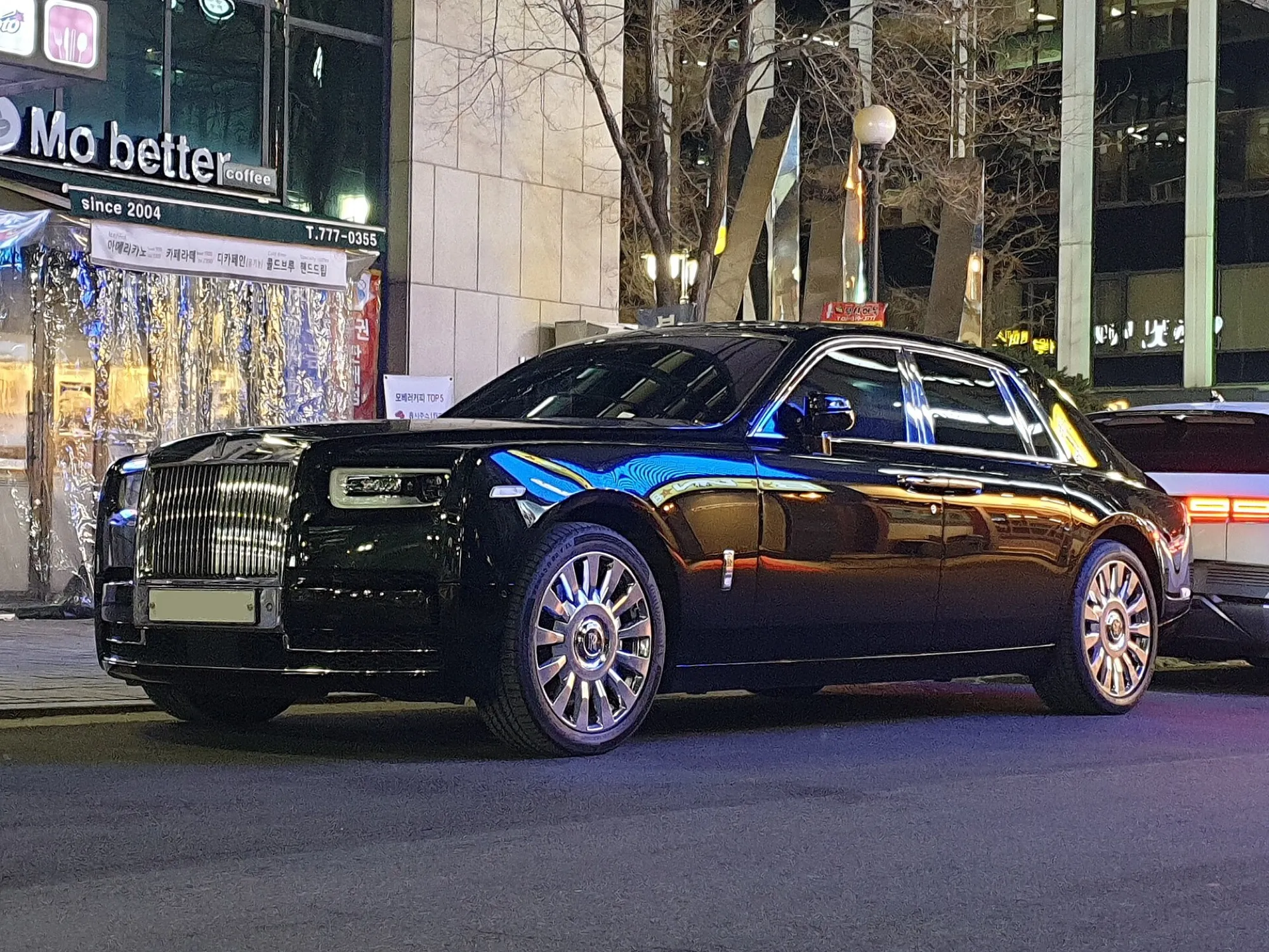 A black Rolls-Royce Phantom saloon seen from the front left on a city street at night