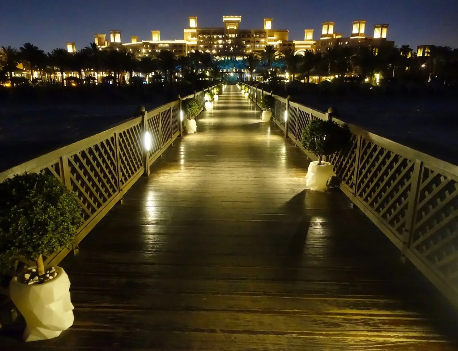 A lit wooden pier leading to the illuminated Madinat Jumeirah resort at night