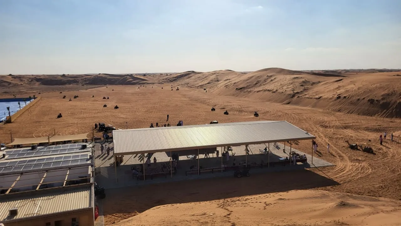 Quad bikes on a wide sand track beside a shaded rental station in the Dubai desert in January