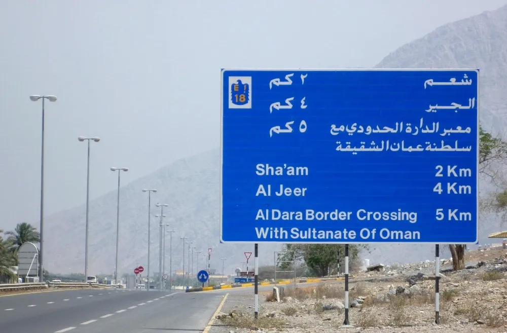 Road sign on the E18 in Ras Al Khaimah giving Sha’am 2 km, Al Jeer 4 km and the Al Dara border crossing with Oman 5 km