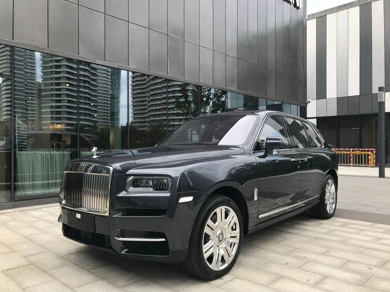 A dark grey Rolls-Royce Cullinan parked outside a glass-fronted building