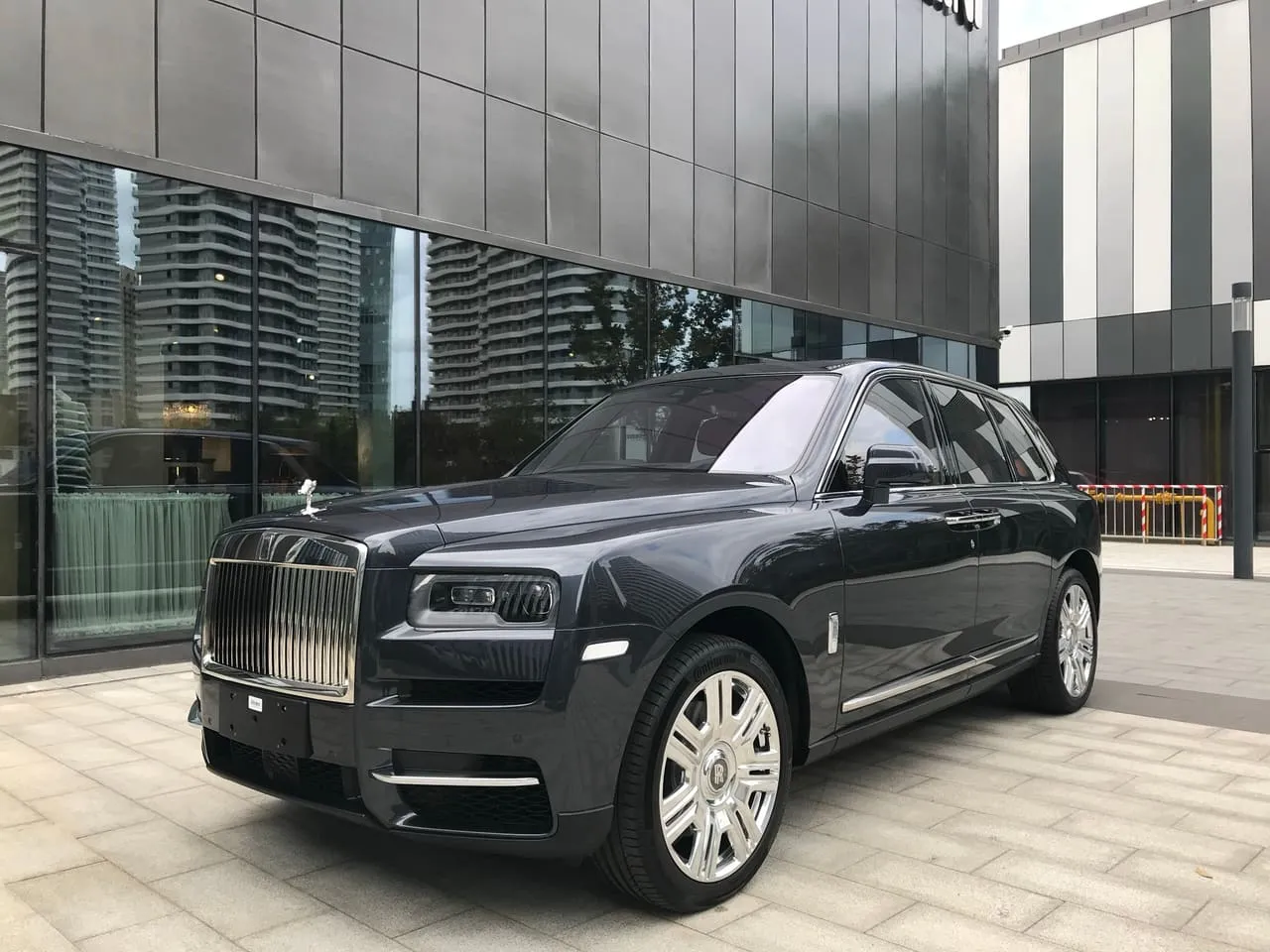 A black Rolls-Royce Cullinan SUV parked outside a glass-fronted building
