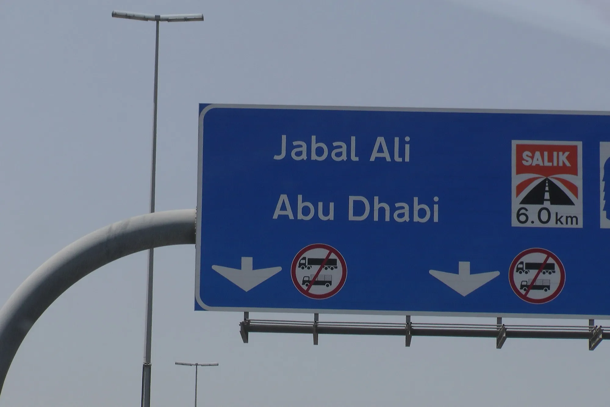 A blue overhead road sign for Jabal Ali and Abu Dhabi with a Salik toll gate warning 6.0 km ahead