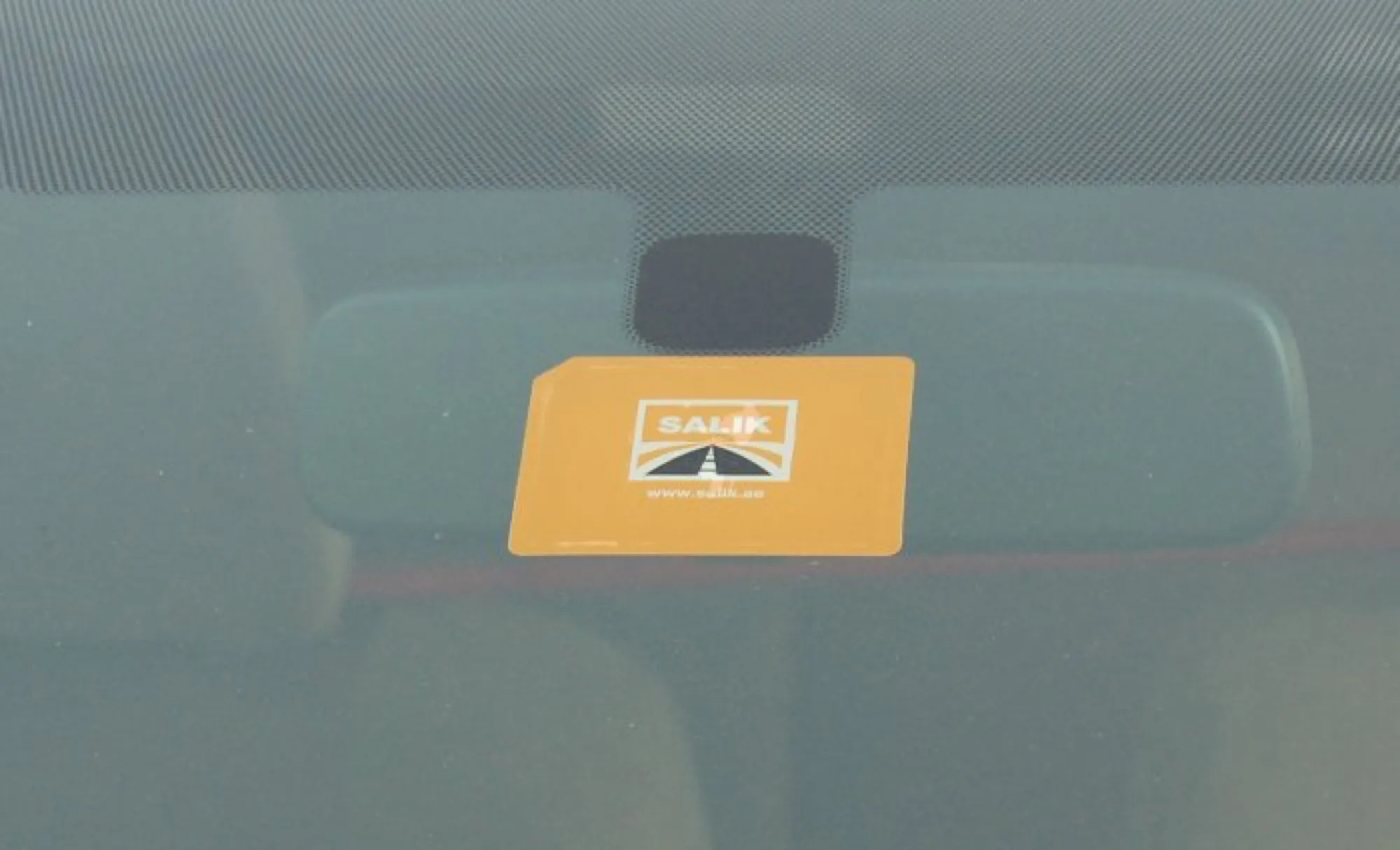 A Salik toll tag stuck to a car windscreen behind the rear-view mirror