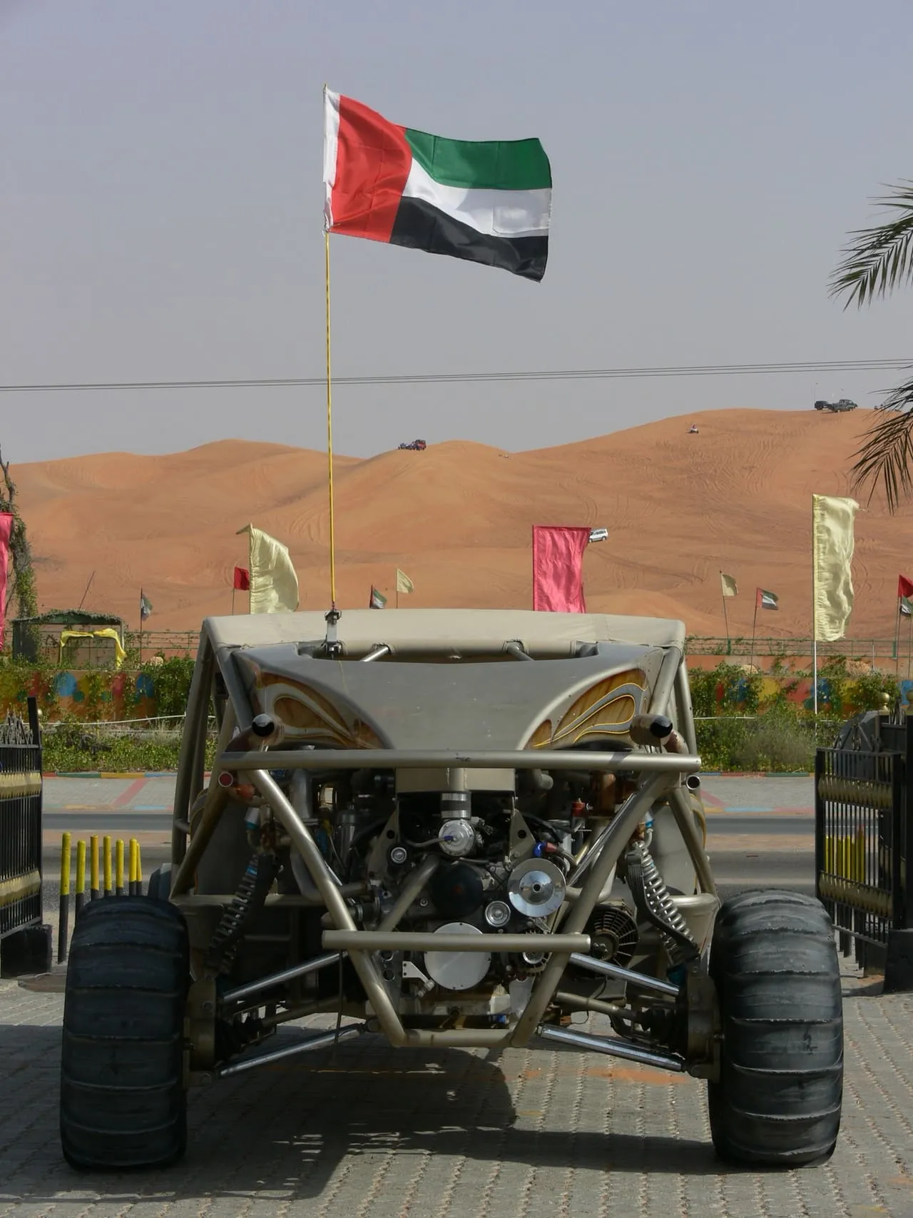A dune buggy with a UAE flag on its mast, parked in front of red dunes in Sharjah