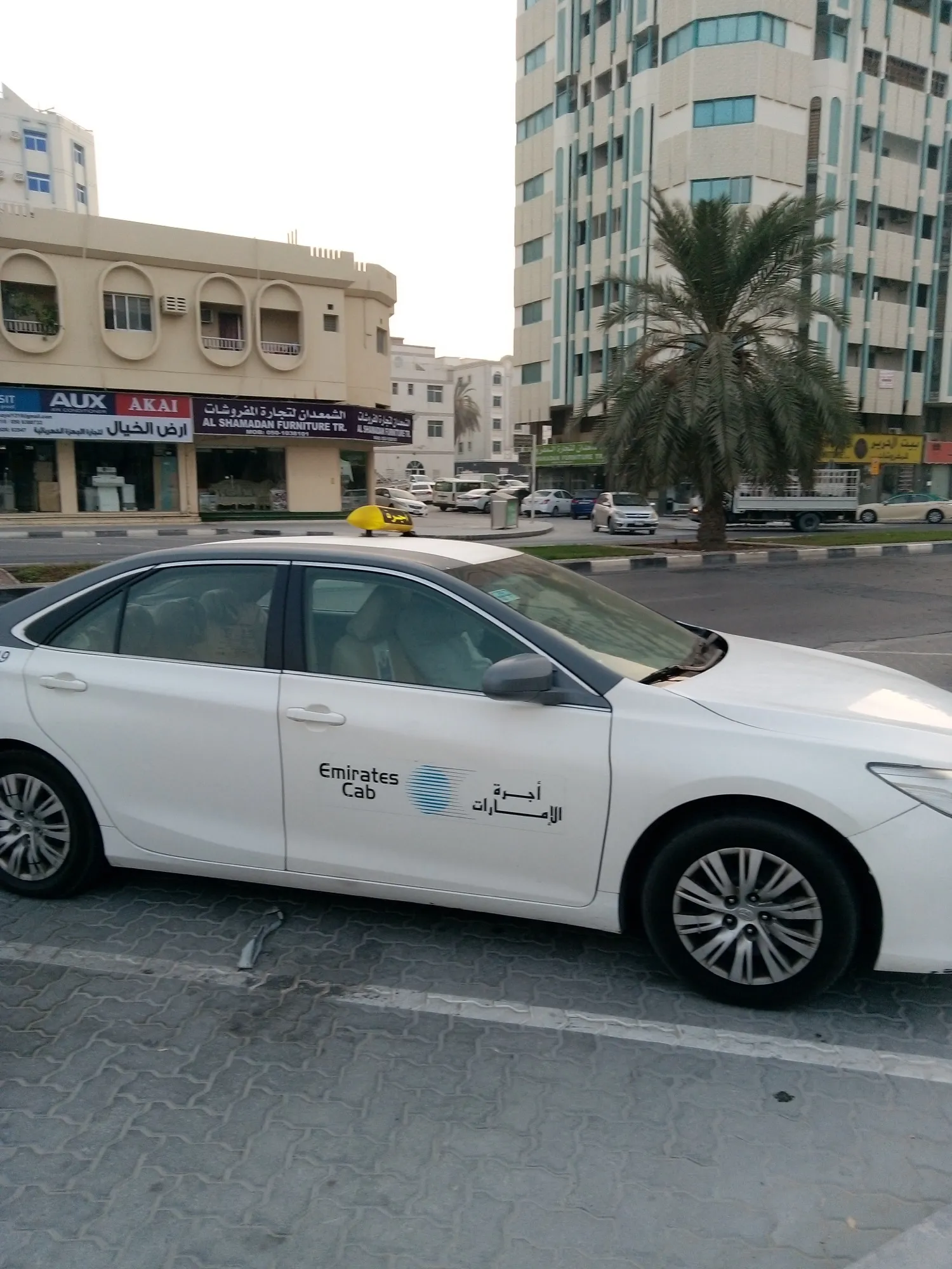 A white Emirates Cab taxi with a yellow roof sign on a Sharjah street