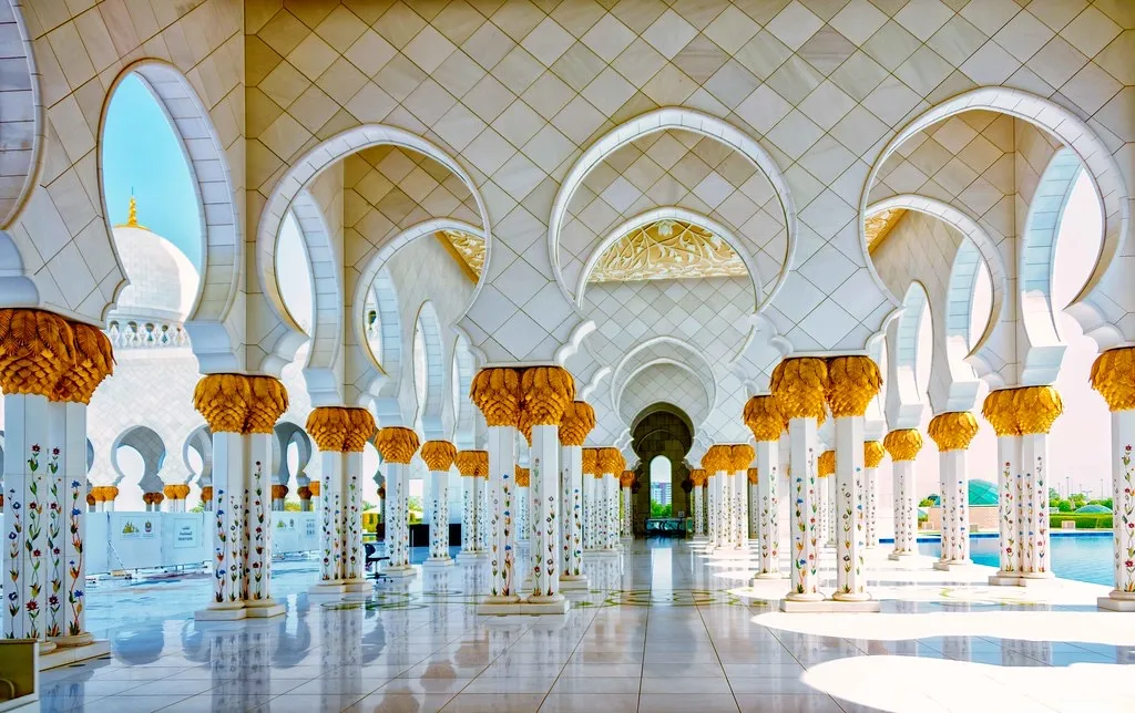 White marble arches and gold-capped columns along a colonnade at the Sheikh Zayed Grand Mosque in Abu Dhabi