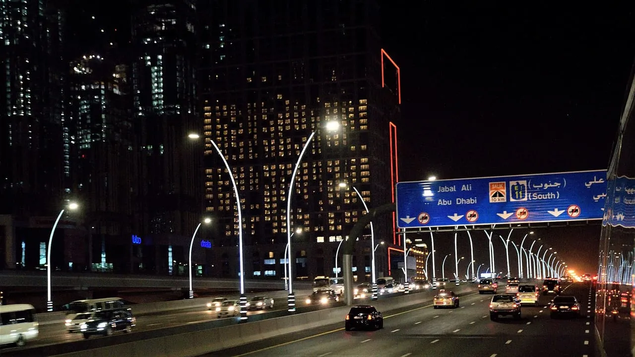 Night traffic on Sheikh Zayed Road in Dubai under an overhead sign for Jebel Ali and Abu Dhabi