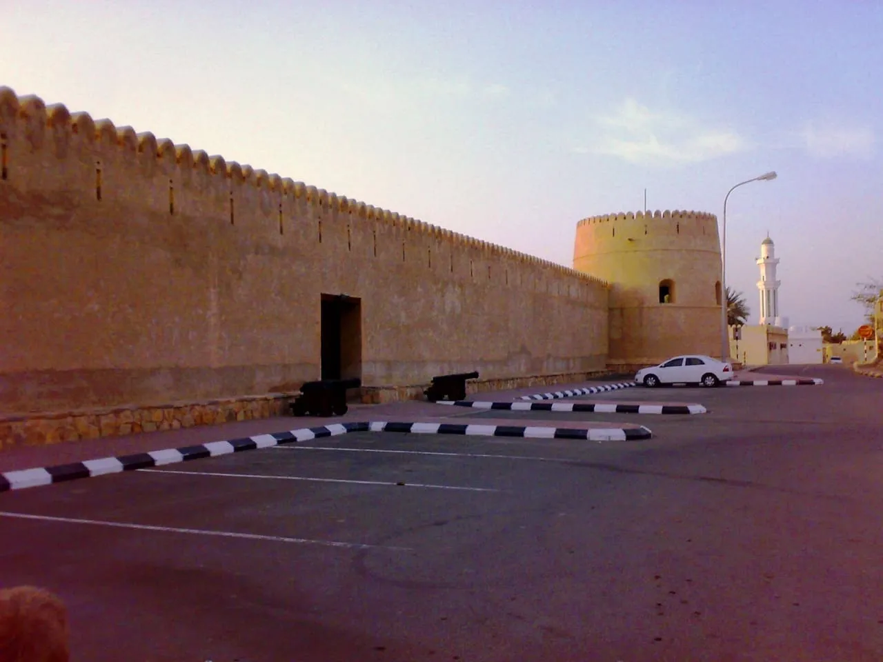 The crenellated walls and round tower of the fort in Shinas, on Oman’s Batinah coast, with a minaret behind