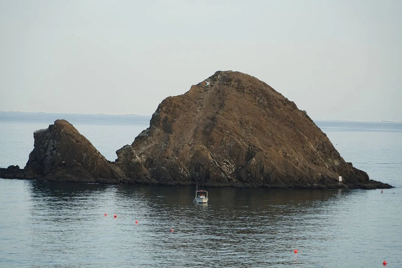 Snoopy Island, a rocky islet off Al Aqah beach, with a small boat moored in the calm water in front