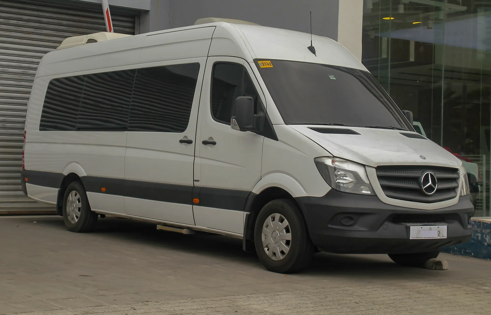 A white high-roof Mercedes-Benz Sprinter minibus with tinted windows and a roof-mounted air conditioning unit