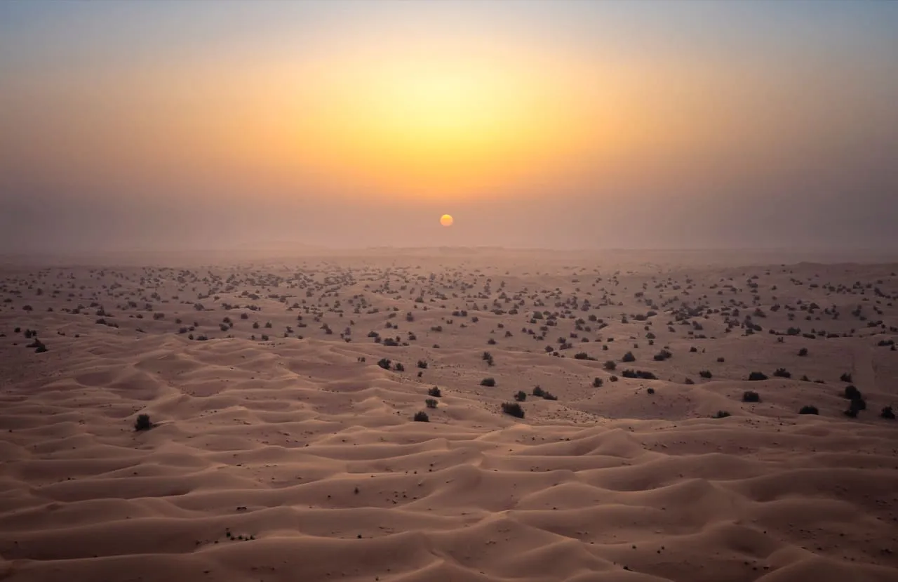 The sun rising through haze over the dunes of the Dubai Desert Conservation Reserve, seen from the air
