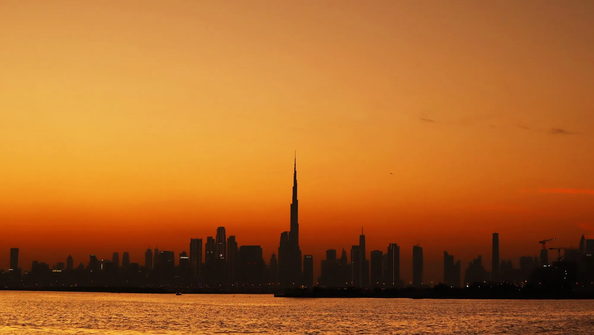 The Burj Khalifa and the Dubai skyline in silhouette at sunset across the water