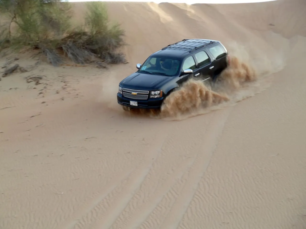 A black SUV throwing up sand as it drives down a dune in the Dubai desert