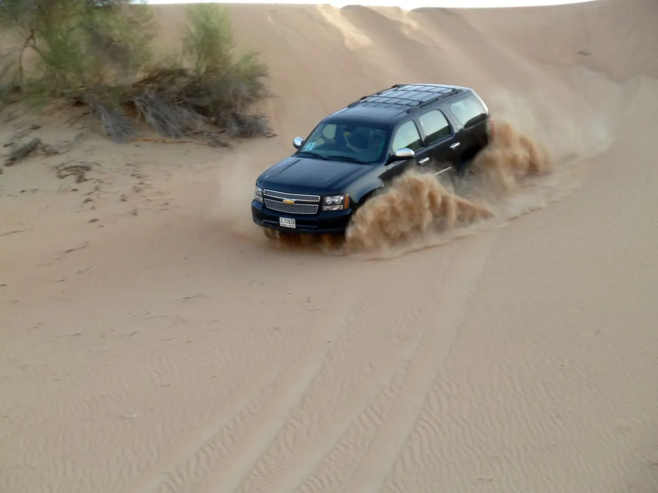A black SUV throwing up a spray of sand as it climbs a dune on a Dubai desert safari