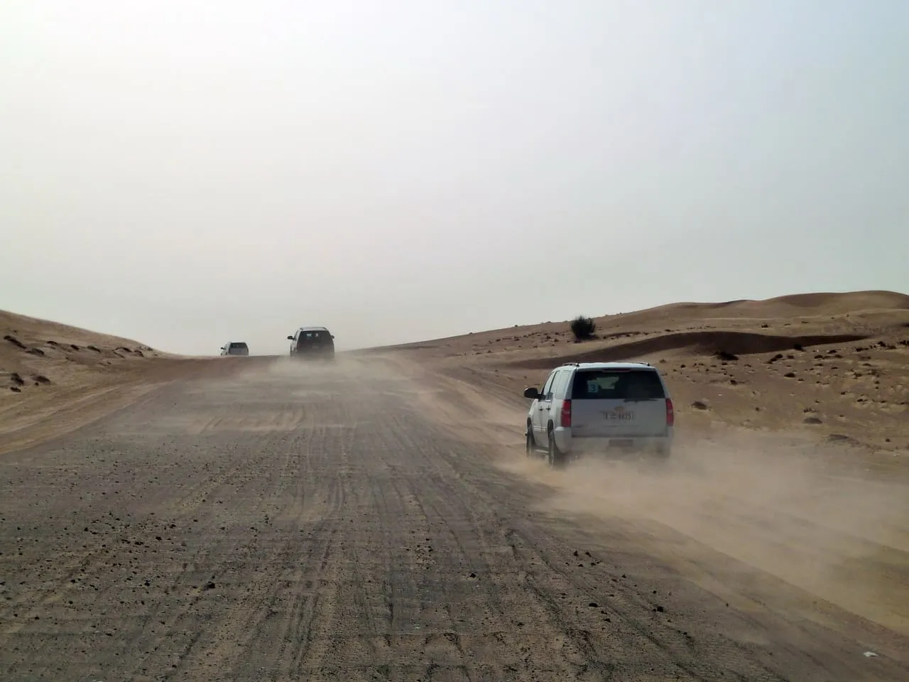 Safari SUVs driving one behind another along a dusty sand track into the desert outside Dubai