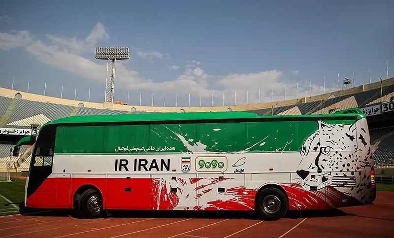 A green, white and red national football team coach parked on the track beside a stadium pitch
