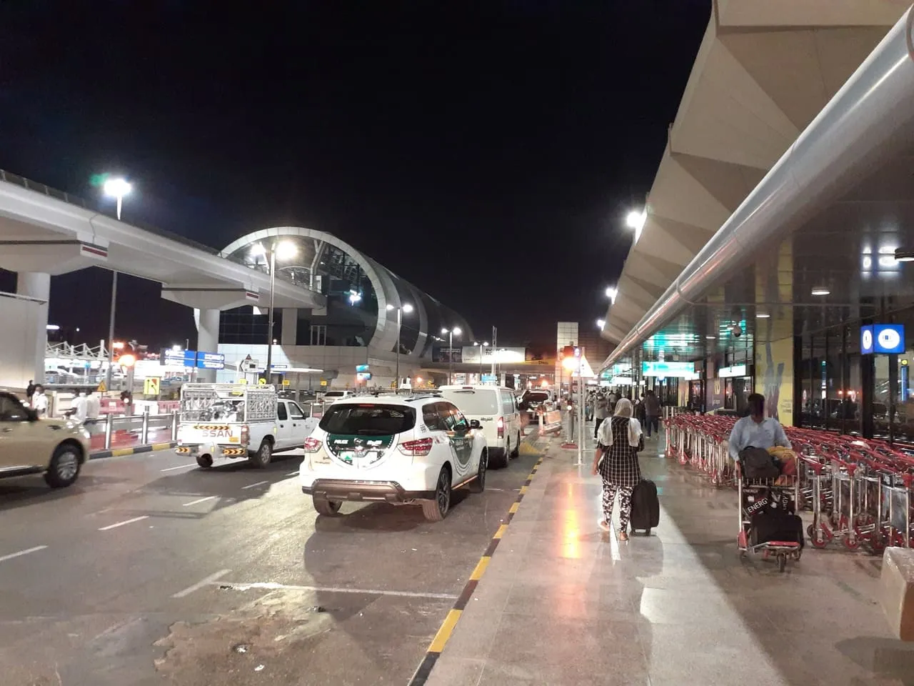 Taxis at the Terminal 1 kerb at night, with the Airport Terminal 1 metro station behind, at Dubai International